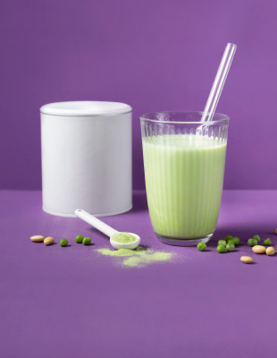 Veganer, grüner Proteinshake im Glas mit Strohhalm und Erbsen
