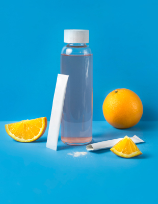 Wasserflasche mit Wasser, daneben Orangenscheiben und ein weißes Pulver-Sachet