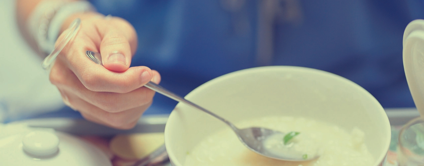 Nahaufnahme einer Hand mit Infusion, die Haferbrei mit dem Löffel aus einer Schüssel isst