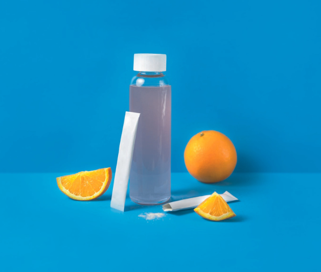 Wasserflasche mit Wasser, daneben Orangenscheiben und ein weißes Pulver-Sachet