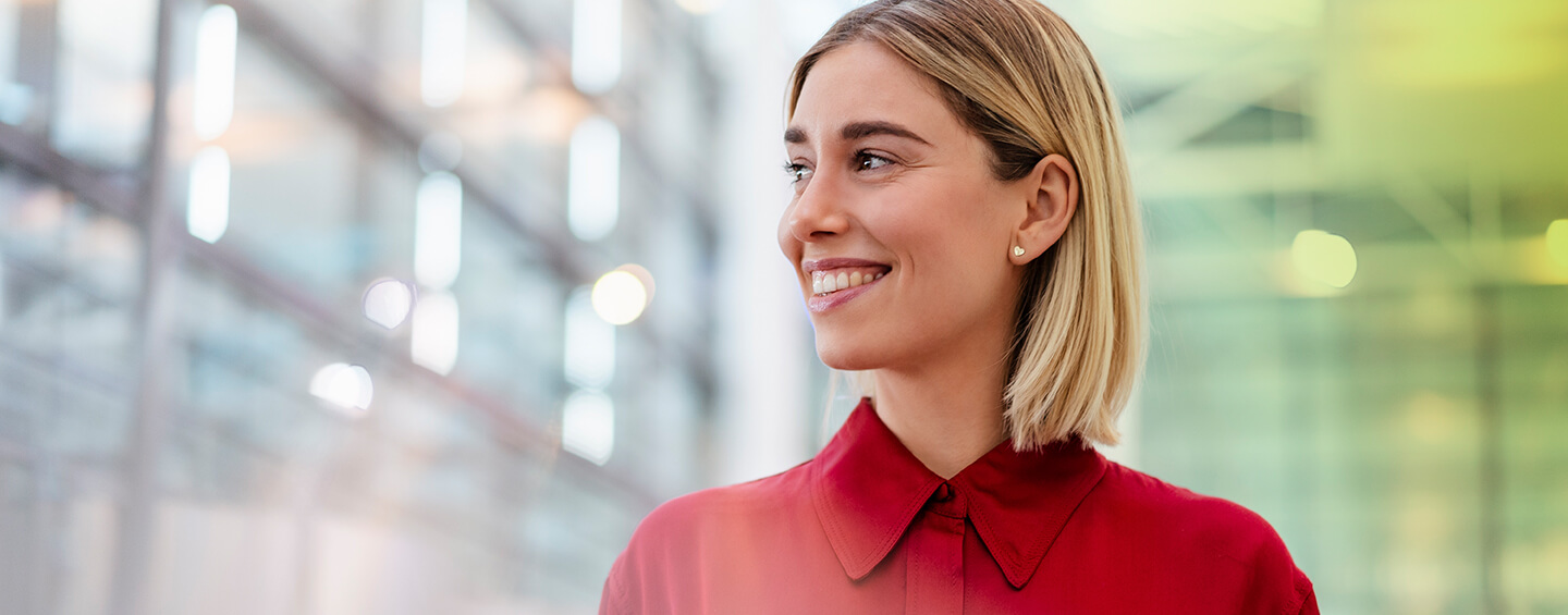 Junge Businessfrau Mitte 20 mit kinnlangen blonden Haaren und roter Bluse schaut fröhlich in die Ferne