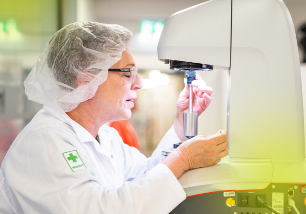 Frau mit Brille und Haarschutz an einem Laborgerät und bei der Untersuchung